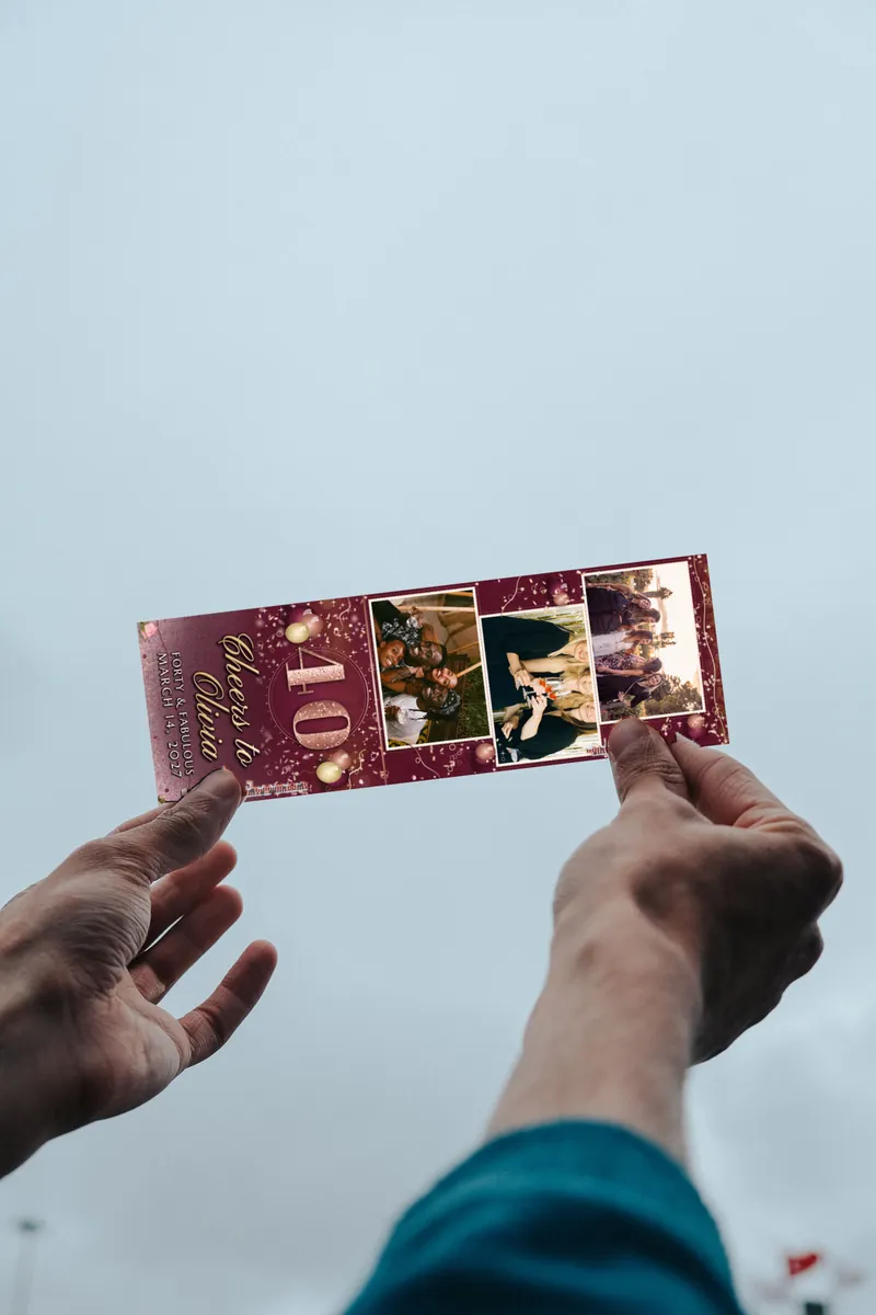 A Rose Gold Forty 2x6 photo strip held up to the sky in two hands